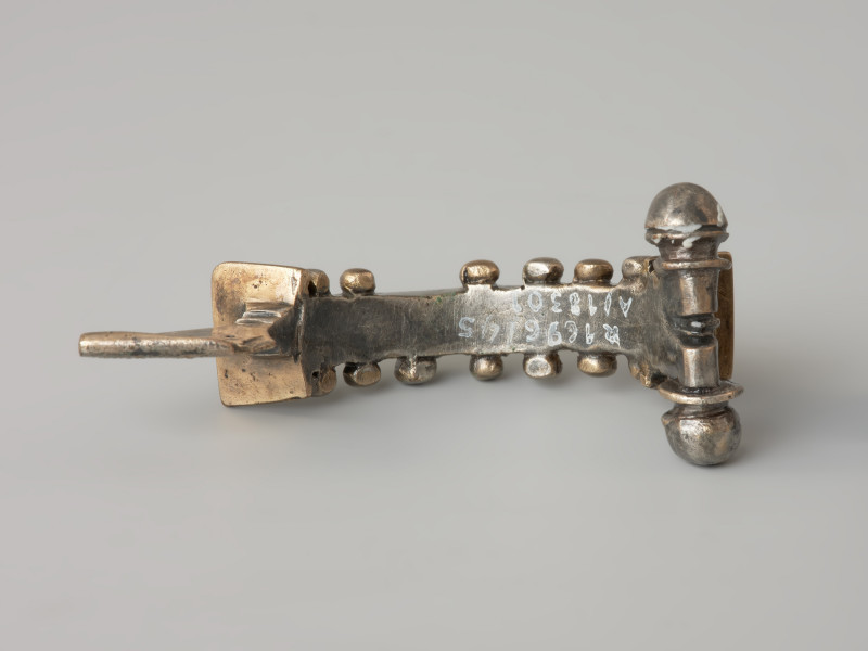 Ujęcie z dołu. Srebrna zapinka z kabłąkiem zdobionym złotymi kulkami.