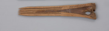 grzebień długi - Ujęcie z przodu. Grzebień wykonano z rozłupanej kości zwierzęcej, prawdopodobnie kości długiej śródstopia bydła. Sześć długich zębów wycięto piłką, a powierzchnię niezbyt starannie ostrugano nożem. Powyżej zębów znajduje się otwór do zawieszania.