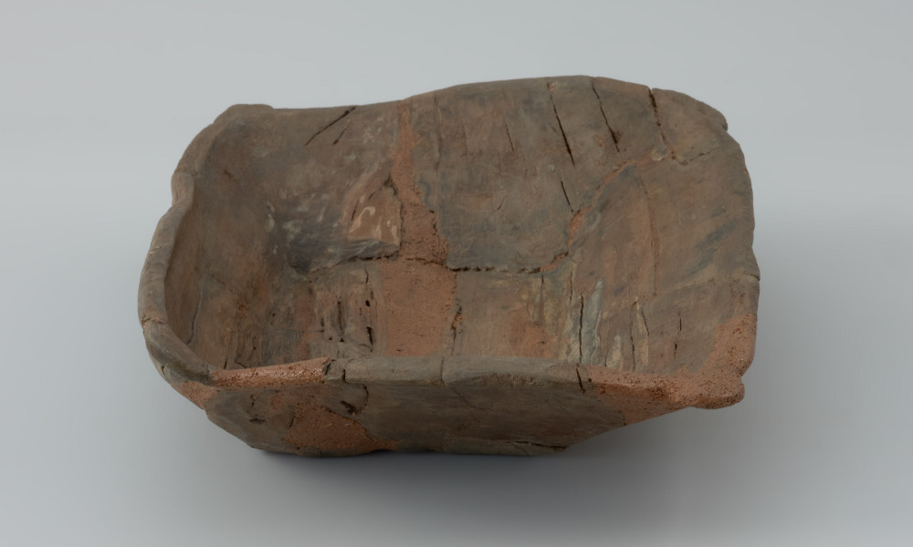 Niecka drewniana; dzieża - Ujęcie lewego krótszego boku dzieży lekko z góry. Płytka niecka wydrążona w przepołowionym pniu drzewa liściastego, zaopatrzona w uchwyty ułatwiające przenoszenie