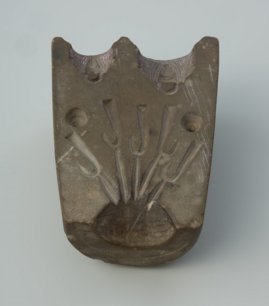 Forma odlewnicza - Ujęcie w pionie brodatymi twarzami do góry.  Jedna część dwudzielnej, kamiennej formy odlewniczej z wizerunkami brodatych twarzy. Wykonano ją ze steatytu zwanego też słoninowcem lub kamieniem mydlanym, który jest miękki i łatwy w obróbce. Zdaniem odkrywców służyć miała do odlewania haczyków do wędek i ciężarków do sieci. Dzisiaj najczęściej uważa się, że jest to forma do odlewu uchwytów niewielkich zawieszek, tzw. osełkowatych lub dzwoneczków. Uwagę zwracają przede wszystkim zróżnicowane wielkościowo wyobrażenia męskich twarzy o migdałowatym kształcie, z dużymi oczami i obfitym zarostem. Po wykonaniu odlewu uzyskiwano przedmiot z wizerunkiem czterech twarzy, uważany za okucie niewielkiej osełki. Forma jest starannie wykonana i nie ma żadnych śladów użytkowania.