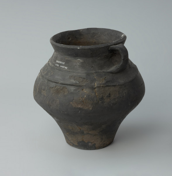 Dwuuche naczynie - Ujęcie z boku. Dwuuche naczynie o gładkiej powierzchni barwy ciemnobrunatnej, miejscami czarnej.