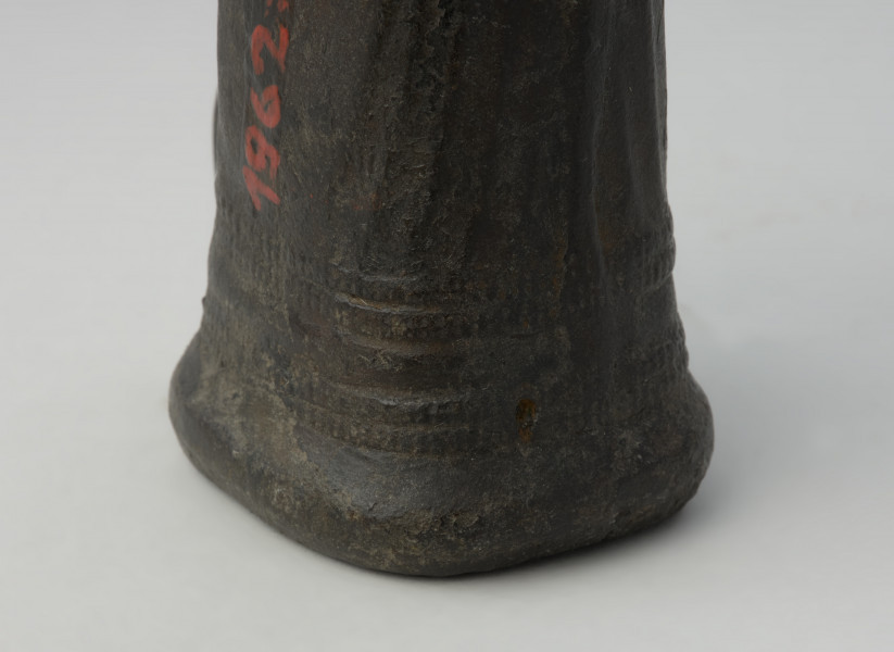 topór, siekiera - Ujęcie detalu zdobionej tulejki od tyłu w pionie. Siekierka brązowa z tulejką i dużym uszkiem, dekorowana żeberkowaniem i karbami przy wylocie tulejki.