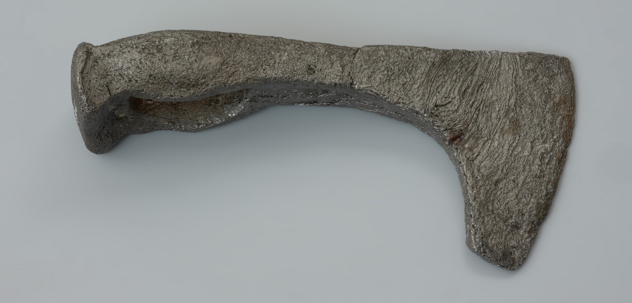 topór bojowy (czekan) - Ujęcie z prawej strony w poziomie. Żeleźce jest masywne, z ostrzem lekko asymetrycznie opuszczonym w stosunku do toporzyska. Obuch jest zakończony krótkim, silnie wyodrębnionym, sztabkowatym zgrubieniem, tak zwanym młotkiem. Szyjka przechodzi w wąskie, asymetryczne i łukowate ostrze zakończone wyodrębnioną, ukośnie podciętą wąską brodą.