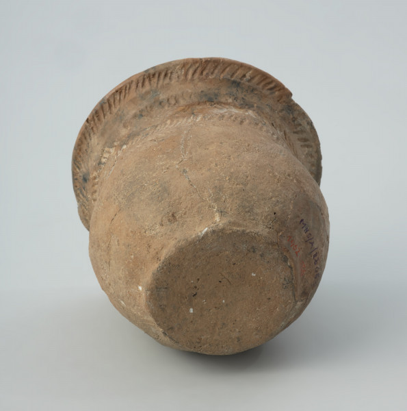 Naczynie gliniane - Ujęcie z dołu; Przysadzisty puchar o szerokim wylewie, zdobiony na szyjce czterema dookolnymi rzędami ukośnych, podłużnych odcisków, które tworzą pasma złożone z dwóch szeregów odcisków układających się w motyw rybich ości. Ukośnymi nacięciami jest zdobiona także krawędź wylewu.