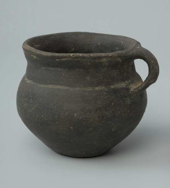 Ujęcie z przodu. Niewielka brunatna waza gliniana o wygładzanej powierzchni.