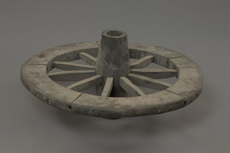 koło - Ujęcie przodu lekko do góry. Replikę koła szprychowego wykonano na podstawie znalezisk z badań wykopaliskowych na Starym Mieście w Kamieniu Pomorskim. Jest produktem kołodzieja, inaczej stelmacha, rzemieślnika zajmującego się wyrobem wozów drewnianych. Poszczególne elementy koła zrobione są z różnych gatunków drewna.