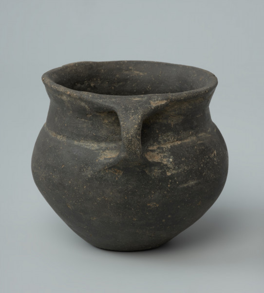 Ujęcie z tyłu. Niewielka brunatna waza gliniana o wygładzanej powierzchni.