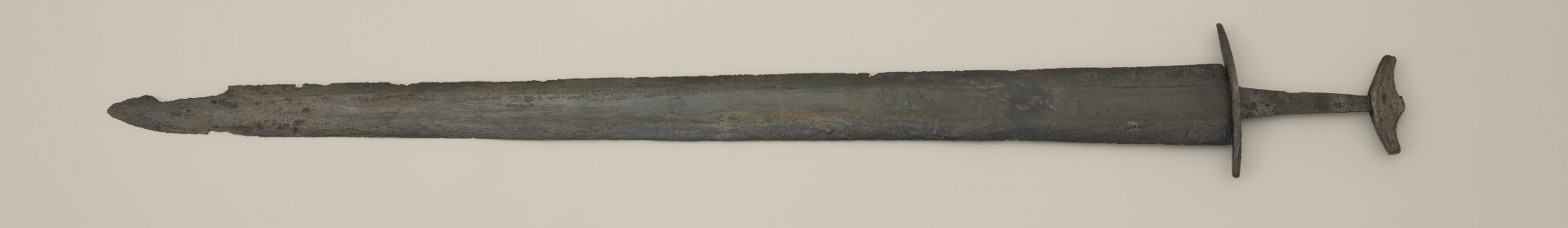 miecz dwusieczny - Ujęcie z tyłu. Całkowicie zachowany, z niewielkimi ubytkami korozyjnymi w okolicach sztycha. Jego głownia jest najszersza przy jelcu i równomiernie zwężą się ku ostremu sztychowi. Jest zaopatrzona w szerokie zbrocze. Głownię wykonano w technice prętowej, poprzez zgrzanie stalowych nakładek ostrzowych z jednolitym rdzeniem. Trzpień mocno zwęża się ku głowicy. Jelec, soczewkowaty w rzucie z góry, jest długi i płaski, a jego końce są zakrzywione w kierunku głowni. Jednolita głowica ma kształt siodełkowaty. Jej dolna część wygięta jest ku górze. Na jej powierzchni zaznaczono symboliczny podział na podstawę i nakładkę.