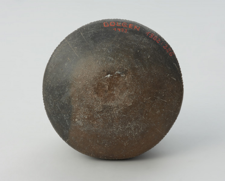 Dwuucha gliniana amfora o czarnej, lśniącej powierzchni. - Ujęcie spodu naczynia. Dwuucha glinina amfora o czarnej, lśniącej powierzchni. Posiada wysoką wydzieloną szyjkę, która lekko rozszerza się ku dwustożkowatemu brzuścowi. Naczynie posiada dekorację w formie jodełki, linii rytych oraz ukośnych nacięć.