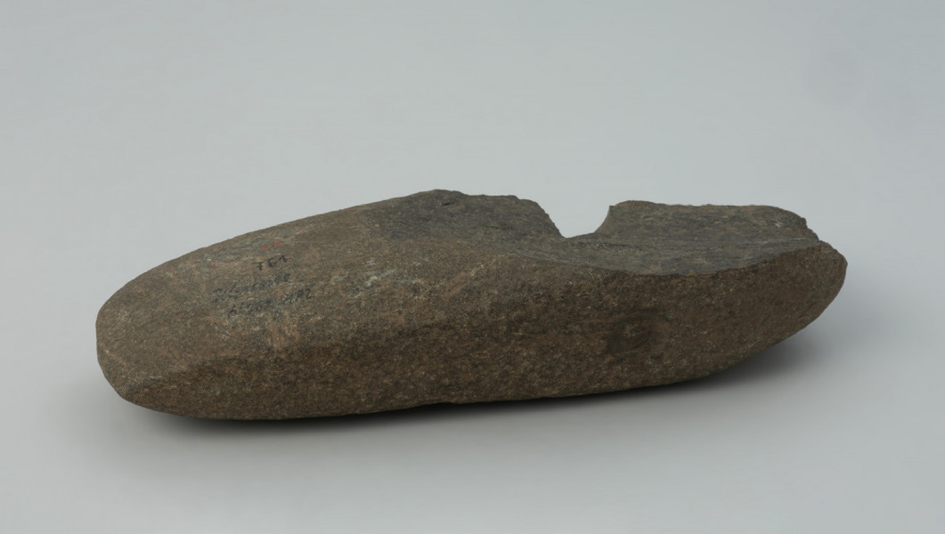 półwytwór, topór - Ujęcie z boku. Półwytwór topora kamiennego z prostym korpusem, pękniętym w trakcie wiercenia otworu w części tylnej. W przekroju otworu zaczątkowego widoczny fragment czopu powstającego przy wierceniu pustym wiertłem