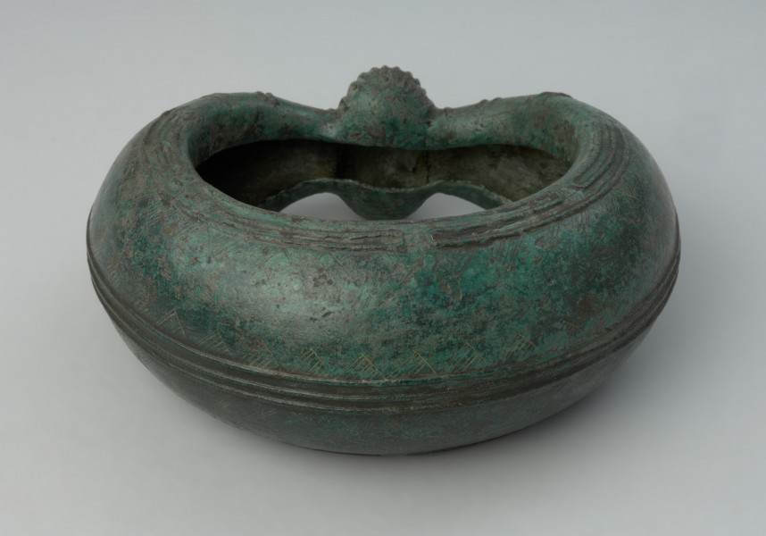 Brązowa bransoleta - Ujęcie z tyłu. Brązowa bransoleta ze zdobieniem w formie gładkich i nacinanych żeberek oraz ryty motyw zygzaków. Na środku znajduje się wypukłość kształtem przypinająca nerkę.