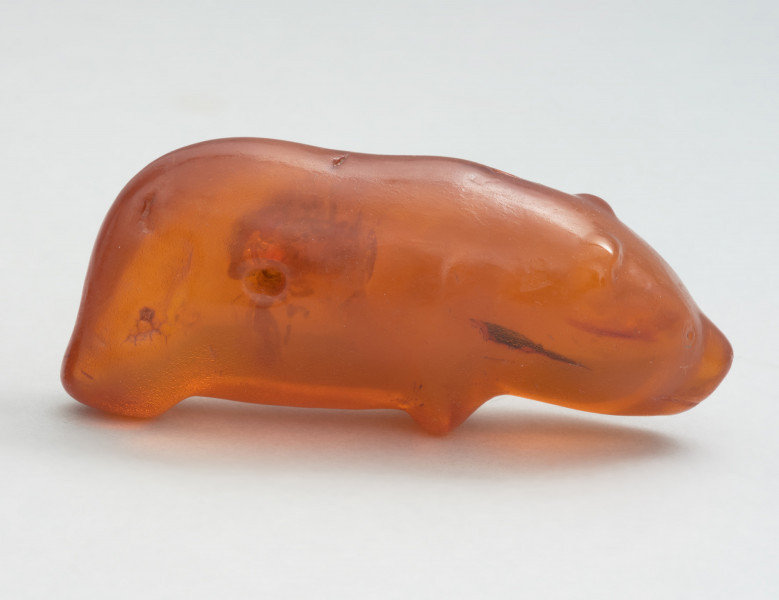 bursztynowa figurka niedźwiedzia ze Słupska - Ujęcie z prawej strony; Bursztynowa figurka niedźwiedzia. Figurka ma schematycznie przedstawiony tułów i nogi oraz realistycznie oddaną głowę. W momencie znalezienia powierzchnia figurki była matowa i spatynowana, jednak krótko po odkryciu przeprowadzono konserwację zabytku. Także ostro zarysowane oczy, usta i nozdrza są wynikiem prac konserwatorskich. Prawdopodobnie oryginalnie miały bardziej schematyczną formę. Figurka posiada dziurę w tułowiu, która jest efektem formowania się bryłki bursztynu wokół gałązki, która z czasem uległa dekompozycji.