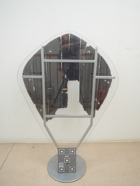 tarcza drewniana - Ujęcie z tyłu, inne światło. Tarcza drewniana, nawiązująca do tarcz typu migdałowatego. Wykonana została z sześciu deszczułek, zwanych też plankami, o szerokości 6,5–17 cm i grubości 0,4–0,7 cm, ściśle przylegających do siebie, spojonych najpewniej klejem pochodzenia roślinnego (żywicznego) lub zwierzęcego (kostnego). Zachowała się jedynie drewniana część tarczy oraz lewy uchwyt skórzany, tak zwany imacz, w postaci paska skóry o długości 42 cm, który przymocowany był za pomocą gwoździ. Po prawym imaczu zachowały się jedynie otwory, podobnie jak po pasie naramiennym. Frontową powierzchnię tarczy pokrywają ślady kolorowej dekoracji namalowanej bezpośrednio na deszczułkach czerwoną, żółtą i czarną farbą. Część centralną zajmuje czerwono-żółty stylizowany krzyż o rozszerzających się ramionach. Wzdłuż brzegu widnieją czerwone kółka i czarne owale z żółtymi rozetami wewnątrz, układające się naprzemiennie, oddzielone od części centralnej czarną kreską.