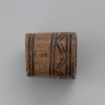 oprawka stożkowata - Ujęcie lewej strony w poziomie. Oprawka ma stożkowaty kształt o ściętym wierzchołku. Ślady pozostawione na jej powierzchni świadczą o wykorzystaniu do jej produkcji co najmniej trzech narzędzi – piły, noża oraz świdra. Na powierzchni oprawki znajduje się mało skomplikowany wzór zdobniczy o motywie liniowym naniesionym za pomocą ostrego narzędzia. Górną część zajmuje ornament w postaci dwóch dookolnych linii rytych. Natomiast na przeciwległej stronie występuje ozdobnik w formie linii zygzakowatych wpisanych od góry i od dołu w podwójne linie ryte.