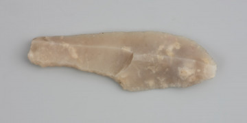 grot; jednozadziorzec - ujęcie z góry; Jednozadziorzec wykonany na wiórze z krzemienia kredowego środkowoturońskiego. Drobna piętka, relatywnie płaski sęczek wióra, płaskie, rozlane fale odbicia, wyraźne skazy promieniste i prosty profil z lekkim podgięciem w części proksymalnej wskazują na odbicie wióra przy pomocy miękkiego tłuka. Na wiórze wyłuskano trzonek, formujący jednocześnie pojedynczy zadzior. Brak retuszu na wierzchołku. Na zabytku brak widocznych śladów użytkowania, możliwe jednak, że zachowały się ślady mikroskopowe. Zabytek pokryty jest lekką jasną patyną, co wskazuje na środowisko depozycji i lekko kwaśnym odczynie.