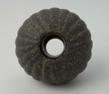 broń; Kamienna buławka melonowata - Ujęcie od dołu. Kamienna buławka melonowata ma kulisty lekko spłaszczony na krańcach kształt oraz pionowe żłobienia. Posiada również przechodzący na wylot otwór.