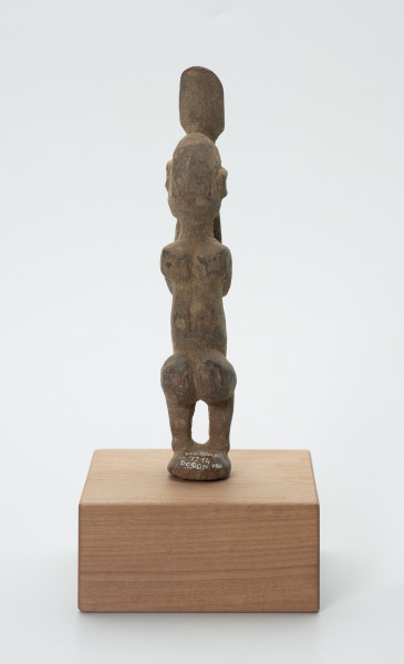 rzeźba - Ujęcie z tyłu. Figura - postać mężczyzny w pozycji stojącej z ugiętym kolanami. Ręce i dłonie nieproporcjonalnie długie/duże w stosunku do całej postaci. Ręce zakrywają twarz, dłonie sterczą ponad głową. Rzeźba związana z kultem przodków.