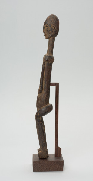 rzeźba - Ujęcie z prawego boku; Figura - postać przodka. Figura antropomorficzna, sylwetka smukła, wydłużona. Ręce krótkie, dłonie ułożone nad pępkiem. Twarz schematyczna w stylu dogońskim. Szerokie biodra. Związana z kultem przodków.