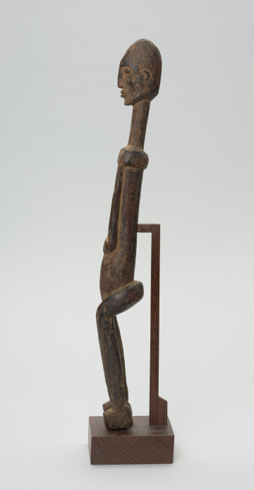 rzeźba - Ujęcie z prawego boku; Figura - postać przodka. Figura antropomorficzna, sylwetka smukła, wydłużona. Ręce krótkie, dłonie ułożone nad pępkiem. Twarz schematyczna w stylu dogońskim. Szerokie biodra. Związana z kultem przodków.