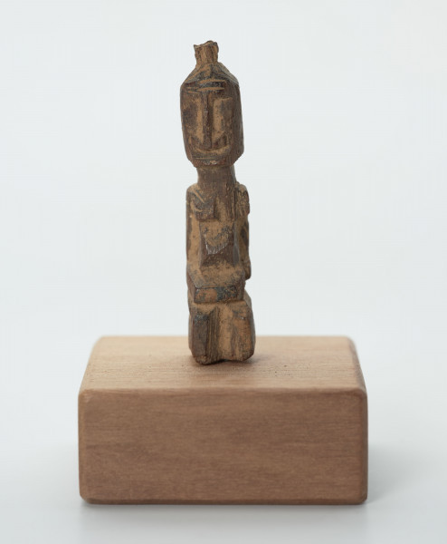 rzeźba - Ujęcie z przodu; Mała figurka antropomorficzna, najprawdopodobniej przedstawienie przodka. Głowa, rysy twarzy, ręce, nogi wydobyte z bryły drewna płytkimi, ostrymi, prostymi cięciami, co nadaje figurce zgeometryzowana formę. Mogła pełnić rolę osobistego fetysza.