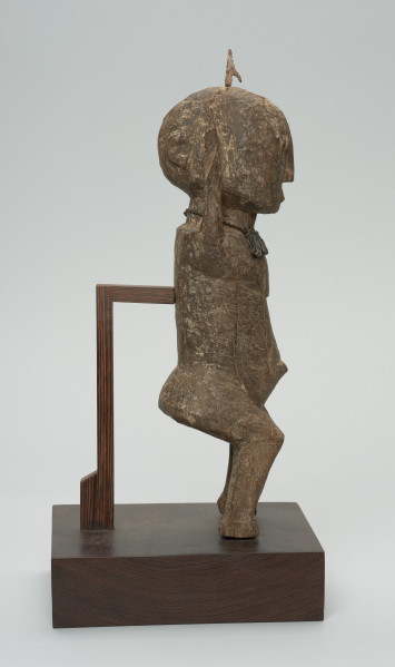 rzeźba - Ujęcie prawego boku. Figura przedstawiająca mężczyznę, o czym świadczy lekko zaznaczony penis. Prawa ręka krótsza od lewej, uniesiona do góry. Ramiona proste, pośladki i uda zaokrąglone. Na głowie wbity kawałek żelaza. Związana z kultem przodków.