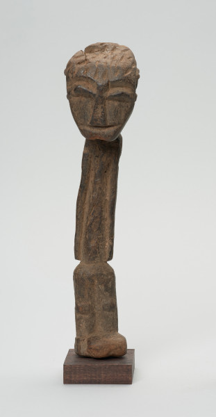 rzeźba - Ujęcie z przodu. Figurka przedstawiająca postać ludzką. Głowa bardzo duża, reszta sylwetki schematyczna, bardzo smukła, lekko wygięta w prawą stronę. Włosy zaznaczone ciosanymi rytami. Nogi wąskie, złączone.