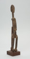 rzeźba - Ujęcie ze skosu z lewej; Figura - postać przodka. Figura antropomorficzna, sylwetka smukła, wydłużona. Ręce krótkie, dłonie ułożone nad pępkiem. Twarz schematyczna w stylu dogońskim. Szerokie biodra. Związana z kultem przodków.