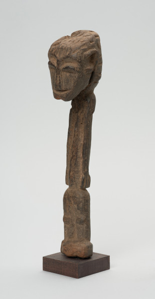 rzeźba - Ujęcie przodu skosem w lewą stronę. Figurka przedstawiająca postać ludzką. Głowa bardzo duża, reszta sylwetki schematyczna, bardzo smukła, lekko wygięta w prawą stronę. Włosy zaznaczone ciosanymi rytami. Nogi wąskie, złączone.