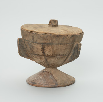 naczynie, rzeźba - Ujęcie z przodu. Drewniane, okrągłe naczynie o kształcie kielichowym na krótkiej, okrągłej nóżce z przykrywką. Całość ozdobiona wzorami geometrycznymi w postaci płytkich nacięć.