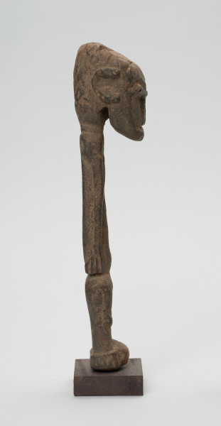 rzeźba - Ujęcie lewej strony. Figurka przedstawiająca postać ludzką. Głowa bardzo duża, reszta sylwetki schematyczna, bardzo smukła, lekko wygięta w prawą stronę. Włosy zaznaczone ciosanymi rytami. Nogi wąskie, złączone.