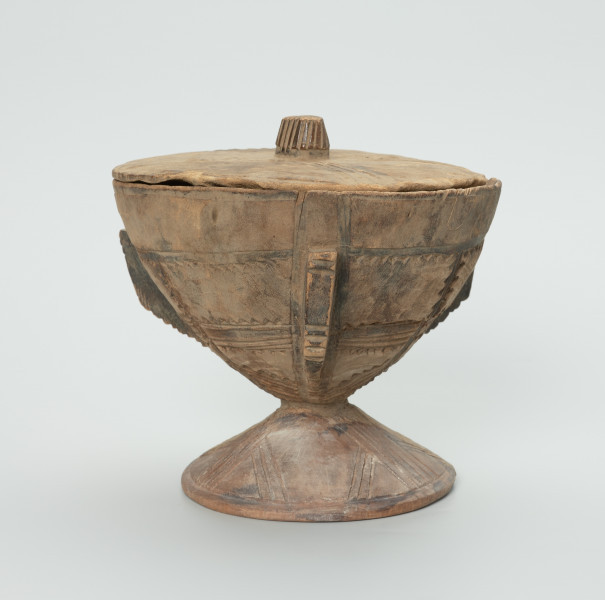 naczynie, rzeźba - Ujęcie z przodu z prawej strony. Drewniane, okrągłe naczynie o kształcie kielichowym na krótkiej, okrągłej nóżce z przykrywką. Całość ozdobiona wzorami geometrycznymi w postaci płytkich nacięć.
