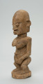 rzeźba - Ujęcie ze skosu z prawej; Figura - postać kobiety w pozycji stojącej. Sylwetka masywna, przysadzista. Głowa duża, z wyrzeźbionymi uszami. Ręce i piersi wydobyte z bryły głębokimi nacięciami. Dłonie ułożone na łonie. Widoczne stopy. Związana z kultem przodków.