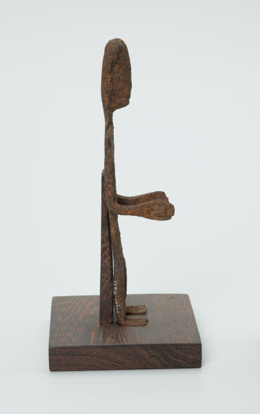 rzeźba - Ujęcie lewej strony. Figurka - postać mężczyzny. Zarysowana tylko sylwetka, ugięte kolana, Ręce zgięte w łokciach. Stanowi wyposażenie grobu.