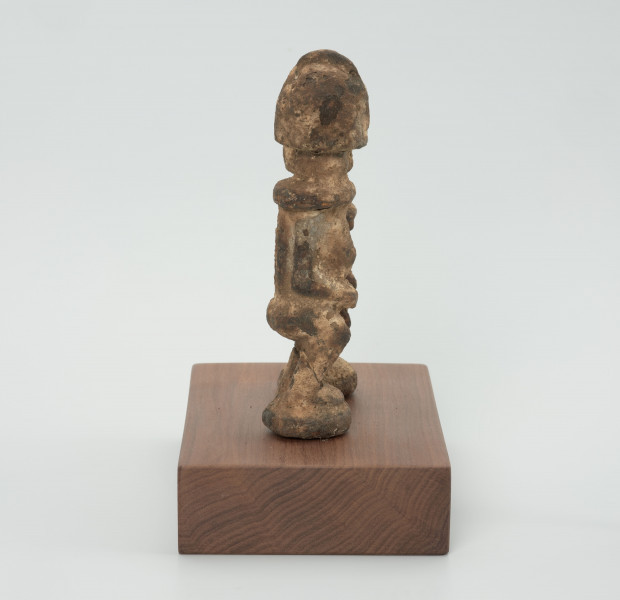 rzeźba - Ujęcie z prawego boku; Zestaw dwóch małych, drewnianych figurek postaci ludzkich w pozycji stojącej, pokrytych warstwą białej i miedzianej substancji. Figurki mają fryzury lub nakrycia głowy postawione na czubku głowy. Widoczne niewyraźne, okrągłe oczy i linia nosa. Ręce rzeźb  przylegają do tułowia, ich dłonie oparto o lekko wypukły i wystający brzuch, nogi krótkie i ugięte w kolanach, stopy połączone, stoją na okrągłych podstawkach. Obie figurki zostały umieszczone przez konserwatora na wspólnej prostokątnej, drewnianej, ekspozycyjnej podstawie.