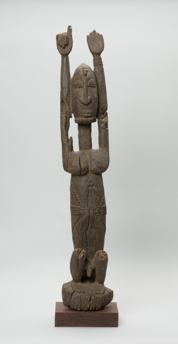 rzeźba - Ujęcie z przodu. Figura - postać mężczyzny w pozycji siedzącej (przykucniętej), z rękoma uniesionymi do góry. Cechy typowe dla dogońskich statuetek: postać statyczna, głowa stosunkowo długa, oddzielona od szyi prostą linią. Nos, usta, oczy wypukłe. Tułów długi, obły. Nogi krótki, schematyczne.