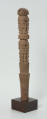 drewniana, rzeźbiona pałka - Ujęcie z przodu, z prawej strony. Okrągła, drewniana pałka z płytko rzeźbionymi dwoma rzędami postaci ludzkich. W każdym rzędzie zaznaczonych zostało czterech przodków, bez wyraźnie zaznaczonych cech płciowych.