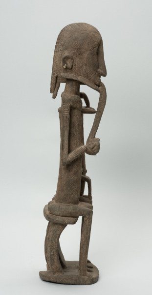 rzeźba - Ujęcie z lewego boku; Figura - para przodków -  mężczyzny i kobiety. Oboje ujęci w pozycji siedzącej. Postacie smukłe. Mężczyzna w ustach ma fajkę, obejmuje lewą ręką kobietę. Związana z kultem przodków.