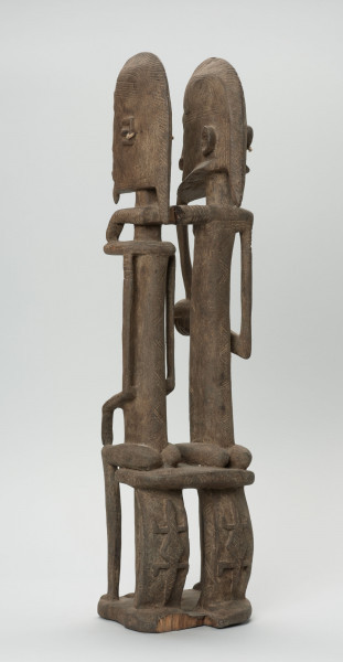 rzeźba - Ujęcie boku i tyłu; Figura - para przodków -  mężczyzny i kobiety. Oboje ujęci w pozycji siedzącej. Postacie smukłe. Mężczyzna w ustach ma fajkę, obejmuje lewą ręką kobietę. Związana z kultem przodków.