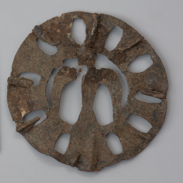 plakietka ażurowa z ptakiem - Ujęcie tyłu plakietki z góry. Metalowa, okrągła plakietka ażurowa z wyobrażeniem ptaka w części centralnej, otoczonego koncentrycznymi kręgami z owalnymi otworami nadającymi całości pewnej lekkości. Na odwrocie plastyczne zeberka ułożone promieniście, wzmacniające konstrukcję.