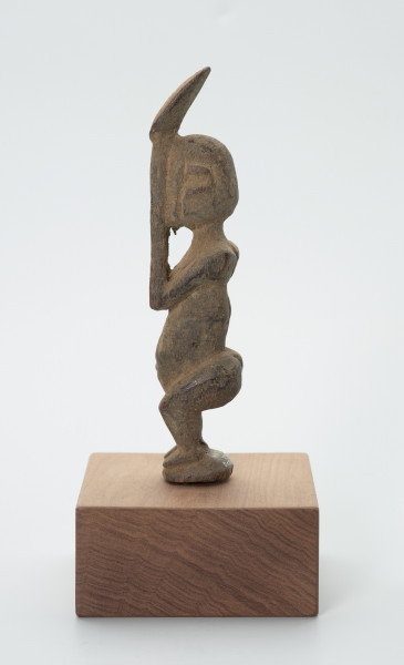 rzeźba - Ujęcie prawej strony. Figura - postać mężczyzny w pozycji stojącej z ugiętym kolanami. Ręce i dłonie nieproporcjonalnie długie/duże w stosunku do całej postaci. Ręce zakrywają twarz, dłonie sterczą ponad głową. Rzeźba związana z kultem przodków.