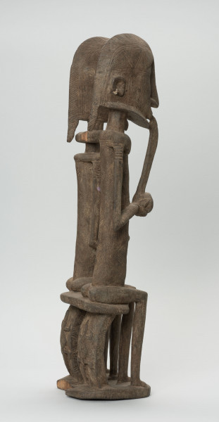 rzeźba - Ujęcie boku i tyłu z prawej strony; Figura - para przodków -  mężczyzny i kobiety. Oboje ujęci w pozycji siedzącej. Postacie smukłe. Mężczyzna w ustach ma fajkę, obejmuje lewą ręką kobietę. Związana z kultem przodków. Krzesełka na których siedzi para rzeźbione z tyłu.