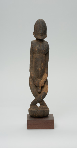 rzeźba - Ujęcie z przodu. Figura przedstawiająca postać przodka -  mężczyznę ze skrzyżowanymi nogami. Figura antropomorficzna, oddająca cechy dogońskiego kanonu przedstawiania ludzi.
