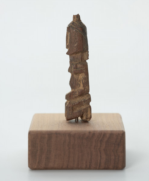 rzeźba - Ujęcie z prawego boku; Mała figurka antropomorficzna, najprawdopodobniej przedstawienie przodka. Głowa, rysy twarzy, ręce, nogi wydobyte z bryły drewna płytkimi, ostrymi, prostymi cięciami, co nadaje figurce zgeometryzowana formę. Mogła pełnić rolę osobistego fetysza.