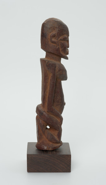 Drewniana figurka mężczyzny z brodą - Ujęcie z prawego boku. Drewniana figurka mężczyzny siedzącego na stołku. Kompozycja zgeometryzowana. Na twarzy zaznaczona broda. Głowa bez włosów.