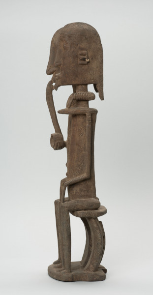 rzeźba - Ujęcie z prawego boku; Figura - para przodków -  mężczyzny i kobiety. Oboje ujęci w pozycji siedzącej. Postacie smukłe. Mężczyzna w ustach ma fajkę, obejmuje lewą ręką kobietę. Związana z kultem przodków.