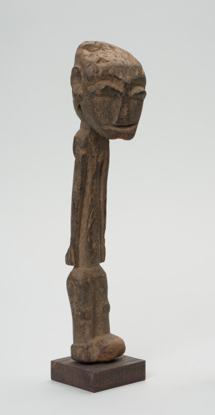 rzeźba - Ujęcie przodu skosem w prawą stronę. Figurka przedstawiająca postać ludzką. Głowa bardzo duża, reszta sylwetki schematyczna, bardzo smukła, lekko wygięta w prawą stronę. Włosy zaznaczone ciosanymi rytami. Nogi wąskie, złączone.