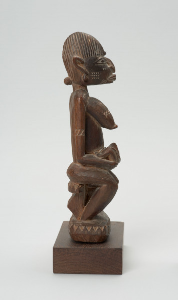 rzeźba - Ujęcie z prawego boku; Figura - kobieta z dziećmi. W obecnym ujęciu widoczna postać kobiety siedzącej bokiem. Kobieta trzyma na rękach niemowle, opierając je na kolanach. Uwydatnione piersi. Bardzo widocznie wyrzeźbione usta, nos, oczy oraz uszy.