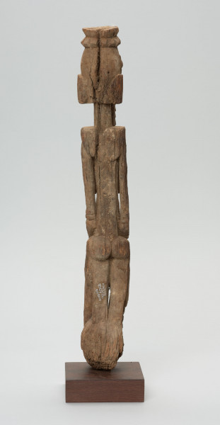 rzeźba - Ujęcie z tyłu; Figura - postać kobiety  - przodka, obdarzona została bowiem ozdobną brodą, czyli pewną cechą męską. Głowa i korpus oddzielone od szyi prostymi cięciami. Oczy duże wypukłe, piersi długie, płaskie, nogi zatarte w wyniku używania. Związana z kultem przodków.