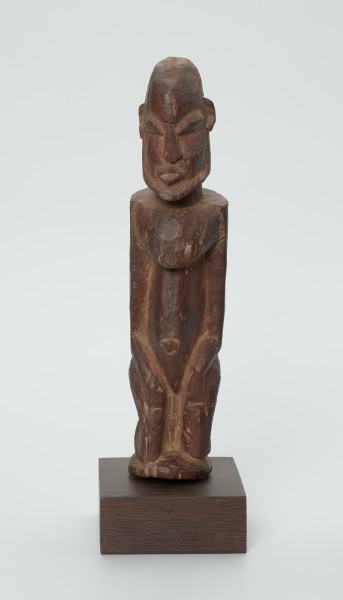 Drewniana figurka mężczyzny z brodą - Ujęcie z przodu. Drewniana figurka mężczyzny siedzącego na stołku. Kompozycja zgeometryzowana. Na twarzy zaznaczona broda. Głowa bez włosów.