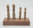 rzeźba - Ujęcie z przodu; Zestaw czterech jasnych, drewnianych figurek przedstawiających postacie ludzkie w pozycji stojącej – dwie kobiety i dwóch mężczyzn. Większa para ma zakryte dłońmi oczy. Rysy twarzy – w postaci oczu, strzałkowego nosa, ust i brody – zaznaczono na mniejszych rzeźbach, których ręce przylegają do tułowia, a dłonie oparto o lekko wypukły i wystający brzuch. Wszystkie rzeźby mają krótkie, ugięte w kolanach nogi. Nie zaznaczono im stóp, w ich miejscu wyrzeźbiono okrągłe podstawki. Wszystkie figurki zostały umieszczone przez konserwatora na prostokątnej, drewnianej, ekspozycyjnej podstawie.